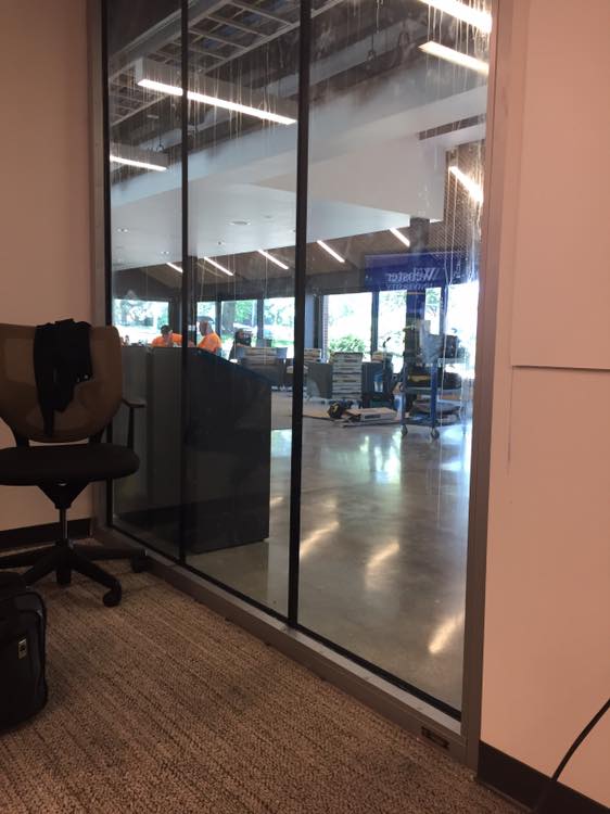 A classroom wall replaced by windows, leaving the instructor visible from the building entrance.