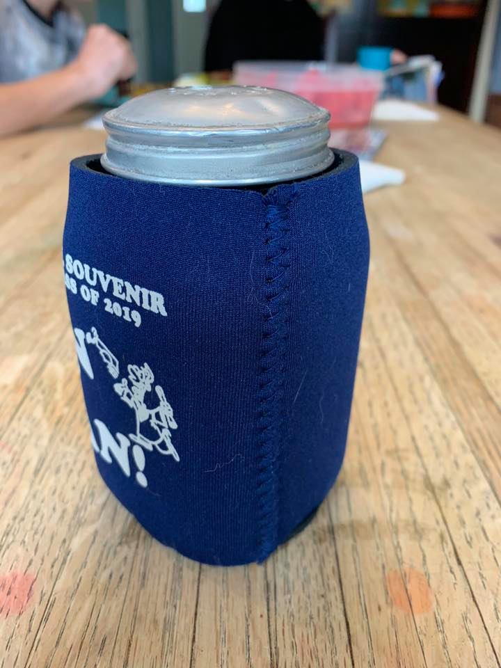 A salt shaker tucked inside a blue souvenir drink coozie on a table.