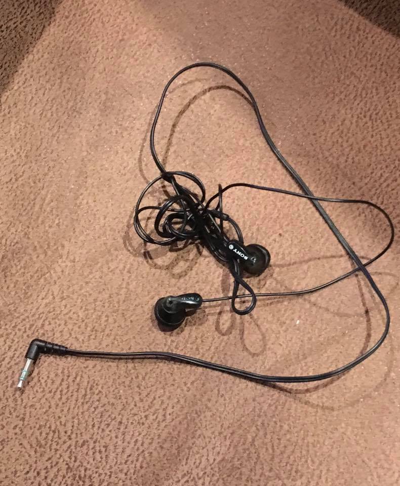 A pair of wired earbuds and cord tightly tangled together on carpet.