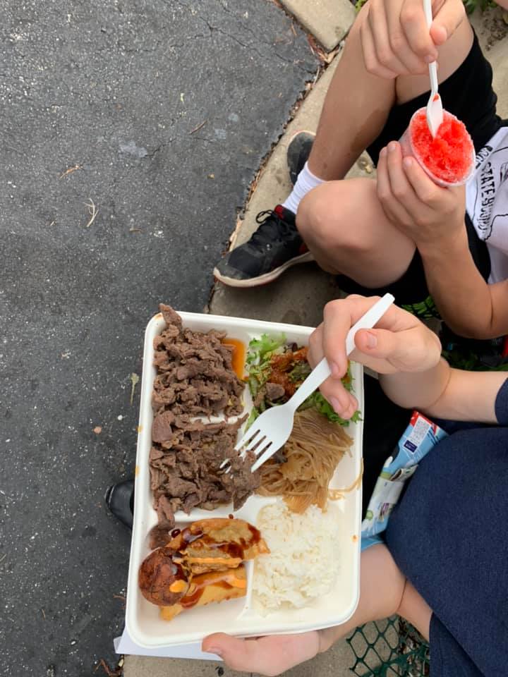Two people eating at the Japanese Festival, one with a tray of food and the other holding a bright red snow cone.