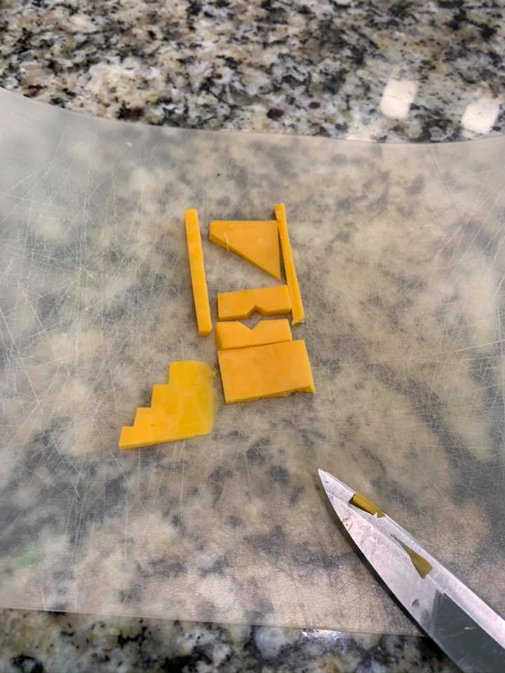 Pieces of cheddar cheese arranged into a small geometric sculpture on a cutting board.