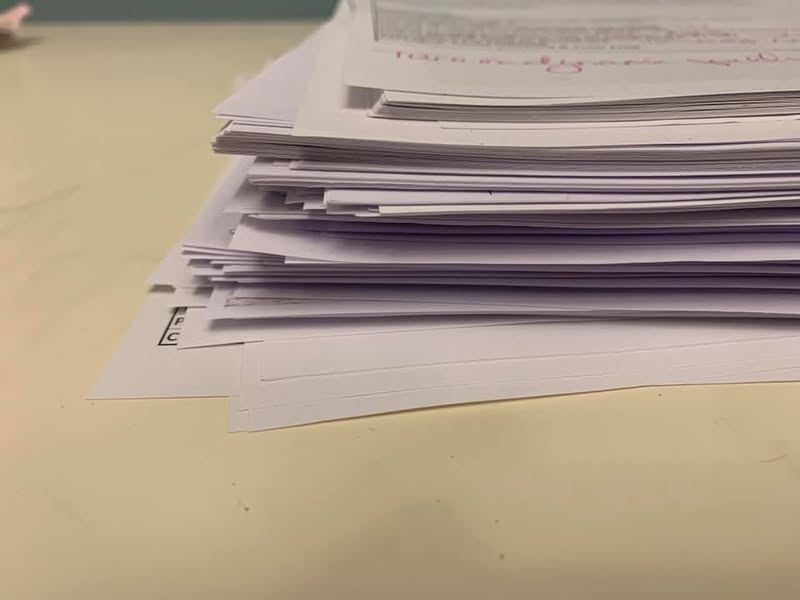 A large pile of printed student design work covered with handwritten feedback and grading notes.