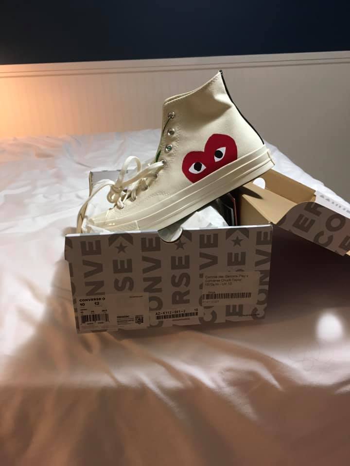 White high-top sneakers with a red heart face logo posed on top of their shoebox.