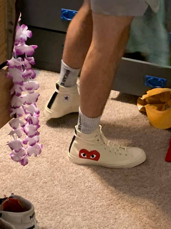 White high-top sneakers with a red heart face logo being worn indoors.