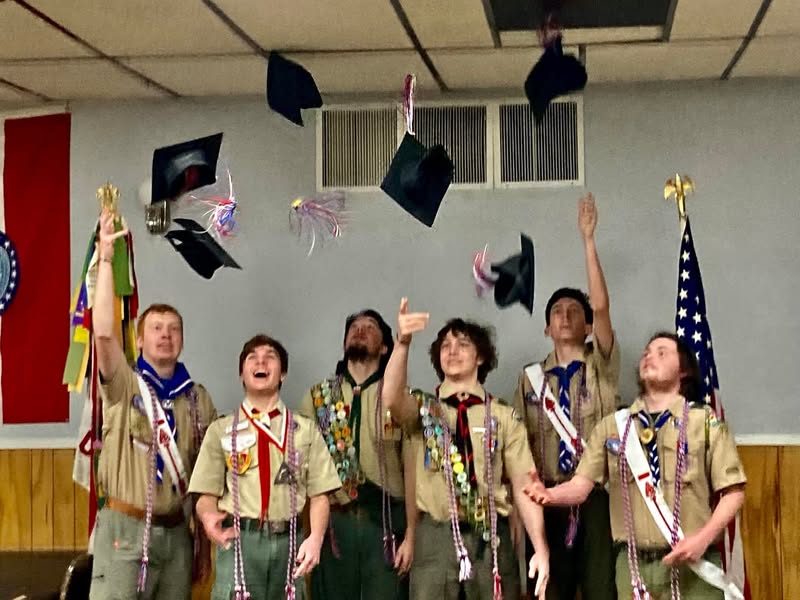 A group of scouts in uniform tossing graduation caps into the air.