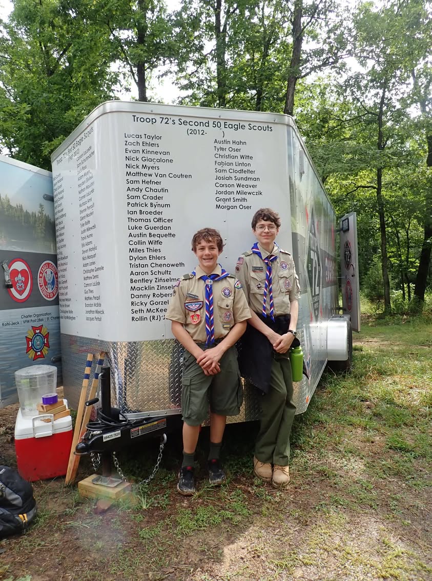 Two scouts standing beside a troop trailer covered with names.
