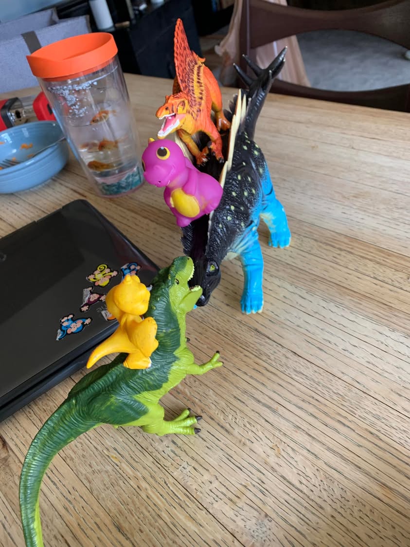 Toy dinosaurs and small figures arranged in a line on a dining table.