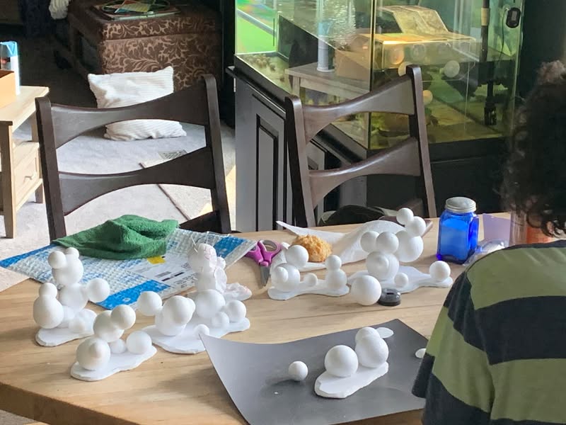 A table covered with many small white sculpted pieces being made for an art project.