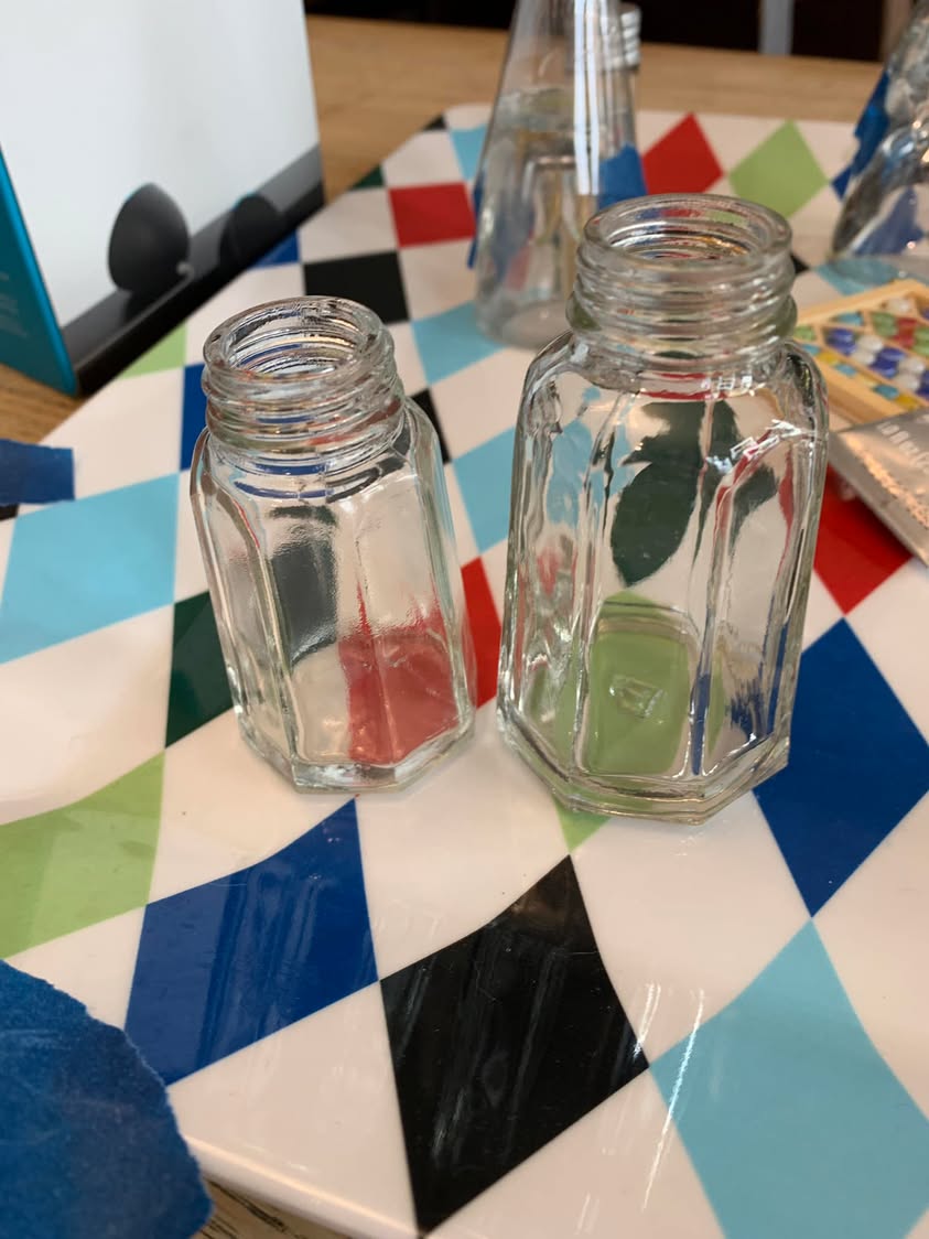 Two glass pepper shakers standing on a colorful patterned tabletop.