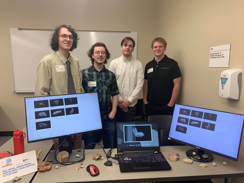 Four student team members standing behind computers displaying their 3D fossil project.