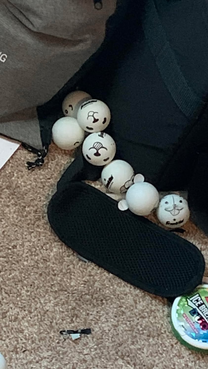A large number of white ping pong balls scattered across a dark floor.