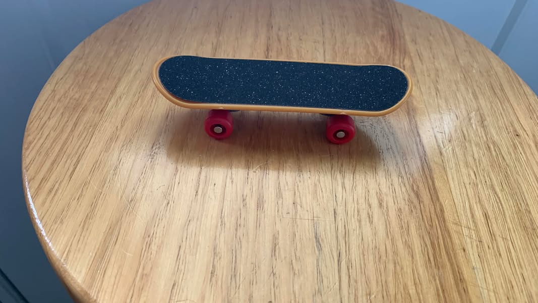 A miniature skateboard with red wheels sitting on a wooden table.