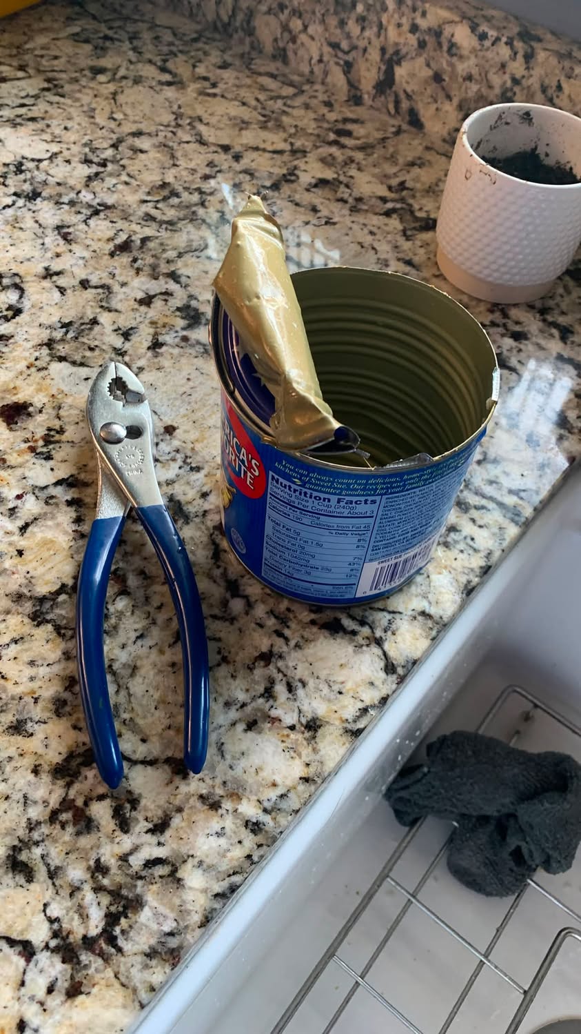 An opened metal can on a kitchen counter beside a pair of blue-handled pliers.